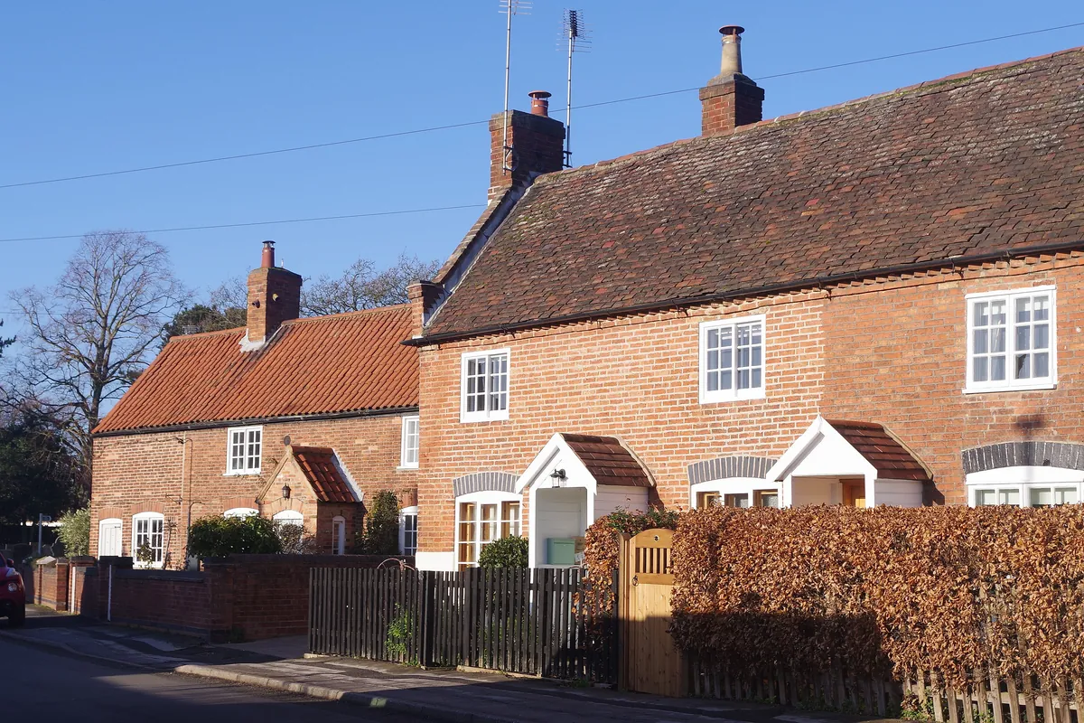 Red-brick cottages with pantile roofs behind a beech hedge in Calverton
